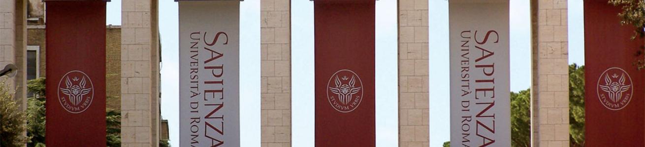 Entrata dei propilei siti all'Ingresso dell'Università di Roma La Sapienza con banner rappresentanti il logo universitario, un cherubino bianco su sfondo rosso e la scritta in verticale Sapienza